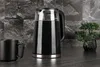A black electric kettle filled with dark liquid sits on a dark countertop next to a black mug and a small potted plant. The background is a textured gray stone wall. Náhled obrázku produktu