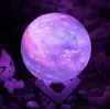 A galaxy-themed moon lamp with a wooden stand, placed on a surface with other decorative items and a plush toy in the background. Náhľad obrázku produktu