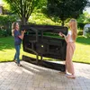 Two women are carrying a folded picnic table in a backyard. Produktbild-Vorschau