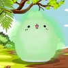 A cartoon-like illustration of a green bunny-shaped night light sitting on a grassy area under a tree. Produktbild-Vorschau