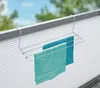 A radiator drying rack with two towels hanging on it, mounted on a white, ribbed surface, with a blurred background of trees and sky. Produktbild-Vorschau