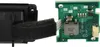 A close-up view of a black foam piece attached to a black plastic component, next to a green circuit board with electronic components and a white connector. Produktbild-Vorschau