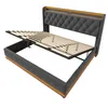 A bed frame with its mattress support slats lifted, revealing storage space underneath. The bed has a tufted headboard and a fabric-covered frame. Produktbild-Vorschau