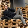 A man is lying on a stack of wooden pallets, talking on his phone. Podgląd zdjęcia produktu