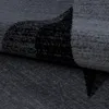 A close-up, angled view of a dark gray rug with a black abstract pattern. Voir les images du produit