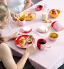 Two people are having breakfast at a table with various food items and colorful tableware. Produktbild-Vorschau