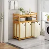 A laundry room scene featuring a bamboo laundry sorter with three beige fabric bins and two shelves holding folded towels and bottles. Anteprima dell’immagine prodotto
