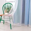 A green chair with a white cup and saucer on it, next to a window with blue and white gradient curtains. Voir les images du produit