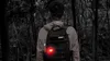 A person wearing a backpack with a red light attached, standing in a dark forest. Podgląd zdjęcia produktu