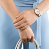 A woman's arms and hands are shown, one wearing a watch, holding a handbag. She is wearing a light blue outfit. Podgląd zdjęcia produktu