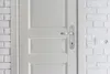 A close-up view of a white door with a silver door handle and a white brick wall with an electrical outlet on the right. Anteprima dell’immagine prodotto