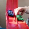 Kinderhand platziert ein grünes Spielzeug-Rennauto auf einer roten Strecke neben einem blauen Spielzeugauto Anteprima dell’immagine prodotto