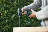 A person is using a cordless drill to drill into a piece of wood outdoors, with greenery in the background. Voir les images du produit