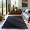 A dark gray rug is placed in a modern living room setting with a sofa, a wooden cabinet, plants, and a large window with a view of nature. Produktbild-Vorschau