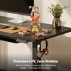 A black standing desk with a computer monitor, keyboard, mouse, and decorative wooden figures. Headphones are hanging from the side of the desk. Produktbild-Vorschau