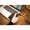 A hand is holding a black external hard drive connected to a laptop. Voir les images du produit