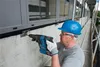 A construction worker is using a Bosch hammer drill to drill into a concrete wall next to a building's facade. Produktbild-Vorschau
