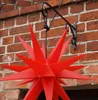 A red star-shaped decoration is hanging from a black metal bracket attached to a brick wall. Produktbild-Vorschau