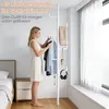 A woman is selecting clothes from a white telescopic coat rack in a bedroom. Produktbild-Vorschau