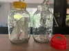 Two glass jars on a wooden table, one with a yellow lid and a plant inside, the other empty with a wooden stick and a red lid nearby. Produktbild-Vorschau