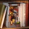 A 3D wooden book nook designed to look like a Japanese street scene, placed between real books on a shelf. Voir les images du produit