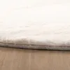 A close-up view of the edge of a fluffy cream-colored rug on a wooden floor. Produktbild-Vorschau
