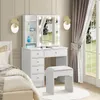 A white vanity table with a lighted mirror and a stool, set up in a bedroom next to a bed and a window with curtains. Voir les images du produit