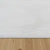A close-up view of a white, high-pile shaggy rug with a scalloped edge, resting on a wooden floor. Voir les images du produit