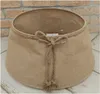 A beige jute Christmas tree skirt with a braided trim and a rope tie in the front, shown from a slightly elevated angle. Voir les images du produit