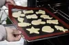 A person is placing a baking mat with cookie dough cutouts into an oven. Podgląd zdjęcia produktu