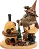 Ein Erzwichtel mit spitzem Hut und buschigem Bart steht neben einem kleinen Holzofen und hält einen Hammer in der Hand während um ihn herum kleine Holzscheite und Tannenzapfen liegen Produktbild-Vorschau