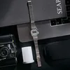A vintage-style digital watch is placed on a dark surface next to a camera and a laptop. Anteprima dell’immagine prodotto