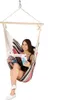 A woman is sitting in a striped hammock chair and reading a magazine. Podgląd zdjęcia produktu