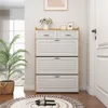 A shoe cabinet with multiple drawers and flip-out compartments, placed in a hallway or entryway next to a potted plant and a door. Náhľad obrázku produktu