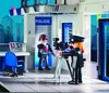 A Playmobil police station scene with two figures, one being photographed by another with a video camera. Produktbild-Vorschau