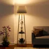A modern floor lamp with shelves is placed next to a sofa in a living room setting. Podgląd zdjęcia produktu