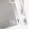 The back of a white and silver heating panel with a power cord and plug attached, lying on a white surface. Voir les images du produit