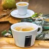 Two cups of espresso coffee on a wooden surface with a pear and some greenery in the background. Voir les images du produit