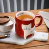 A red mug with a cat design filled with tea, placed on a marble cutting board on a wooden table. Produktbild-Vorschau