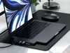 A laptop with a docking station attached, connected to various USB devices, sits on a desk with a mouse and a plant in the background. Produktbild-Vorschau