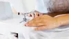 A close-up shot of a person's hands using a white sewing machine to sew white fabric. Podgląd zdjęcia produktu