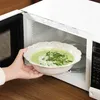 A hand placing a bowl of green soup into a microwave. Produktbild-Vorschau