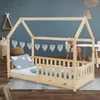 A wooden house-shaped bed for children, set up in a room with a blue wall and a rug on the floor. Produktbild-Vorschau