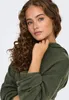 A close-up portrait of a young woman wearing a green sweater. Produktbild-Vorschau