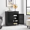 A black shoe cabinet with one drawer and two doors, one of which is open, revealing shelves with items. The cabinet is in a room with a lamp and a picture on the wall. Produktbild-Vorschau