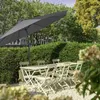 An outdoor patio set with a large umbrella, chairs, and a table, set in a garden with manicured hedges and trees. Produktbild-Vorschau
