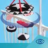 A baby mobile with various patterned toys is attached to a crib railing. A blue arrow indicates rotation. Produktbild-Vorschau