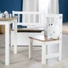 A child's table and chairs set with a storage bench in a room with blue walls and white curtains. Produktbild-Vorschau
