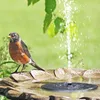 A robin stands on the edge of a bird bath with a solar-powered fountain spraying water. Produktbild-Vorschau