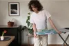 A woman is adjusting an ironing board in a room. Produktbild-Vorschau